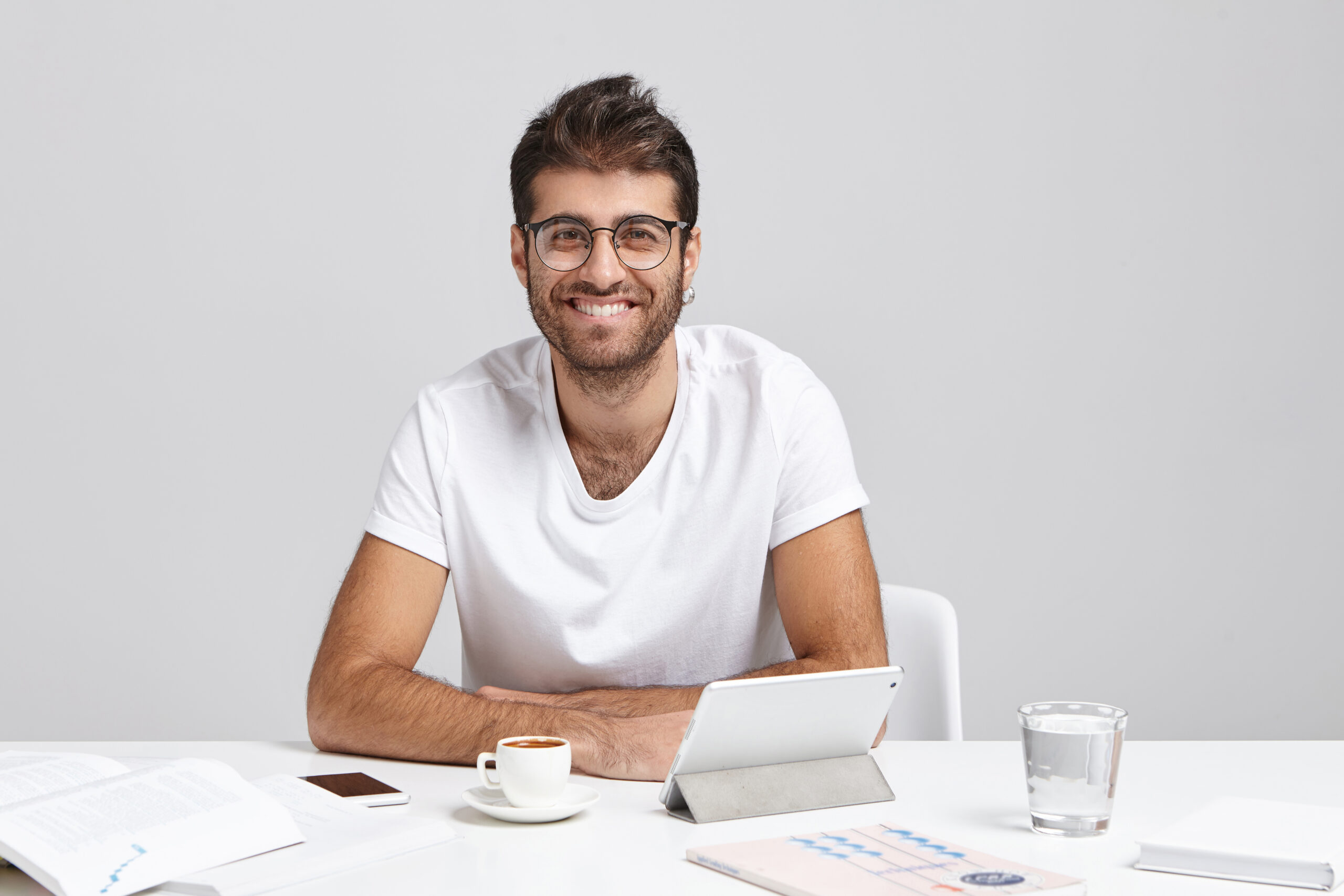 People, success, promotion concept. Fashionable young office worker wears round spectacles and white t-shirt, has broad smile, rejoices his promotion at work, isolated over grey background